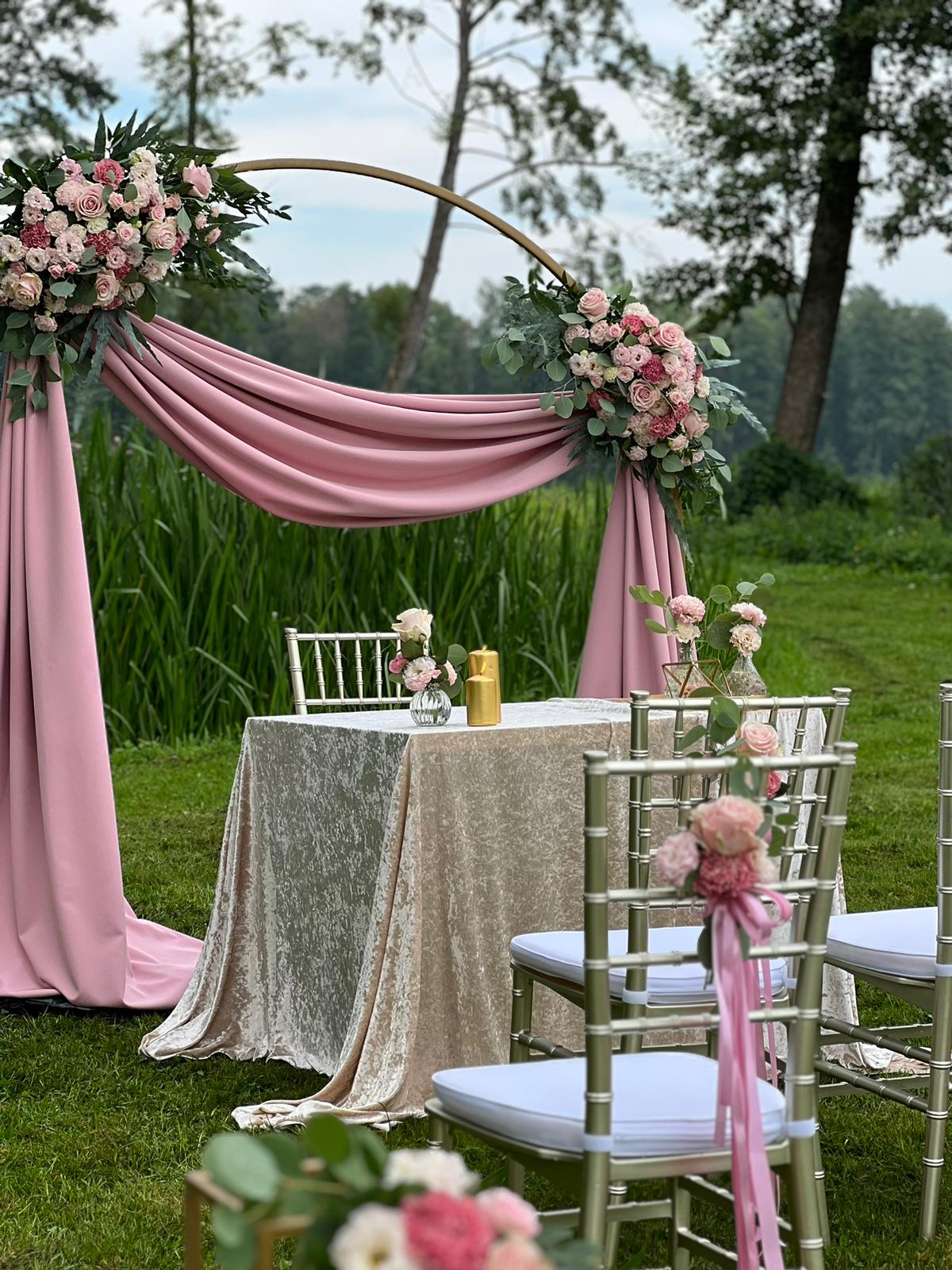 Plenerowa ceremonia ślubna z różowymi draperiami i obręczą florystyczną